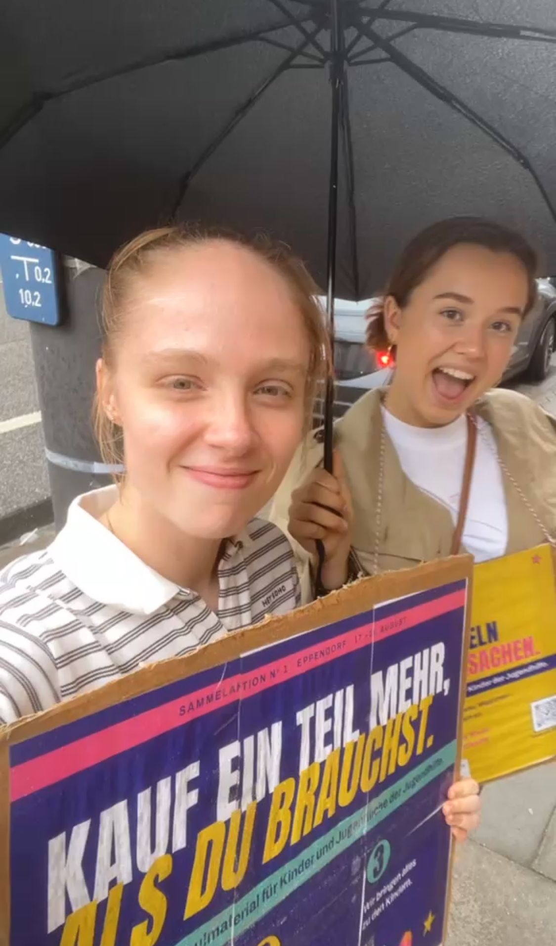 Zwei Freiwillige unter einem Regenschirm mit Plakat